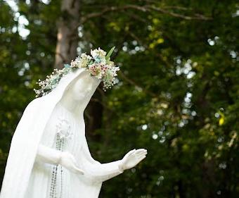 法蒂玛圣母雕像饰有珠子和花冠，背景是绿色的树叶.