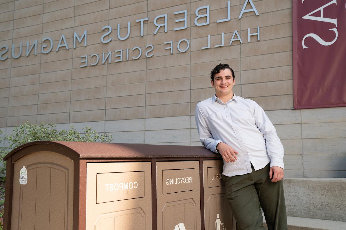 Aidan Donnelly beside waste collection bins outside of Albertus Magnus Hall of Science